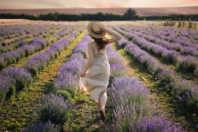 Photo of Woman with straw hat and beautiful flowers running through lavender field