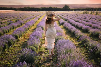 Photo of Woman with straw hat and beautiful flowers running through lavender field