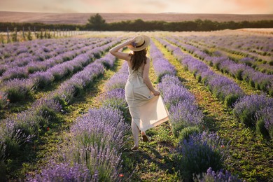Photo of Woman with straw hat and beautiful flowers running through lavender field