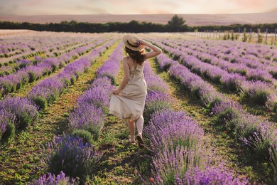 Photo of Woman with straw hat and beautiful flowers running through lavender field