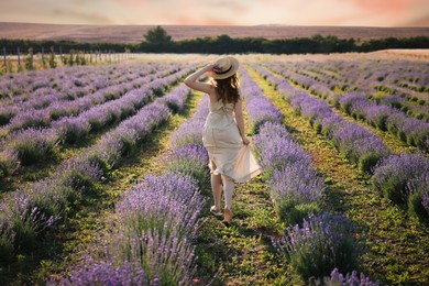 Photo of Woman with straw hat and beautiful flowers running through lavender field