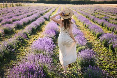 Photo of Woman with straw hat and beautiful flowers running through lavender field