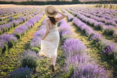 Photo of Woman with straw hat and beautiful flowers running through lavender field