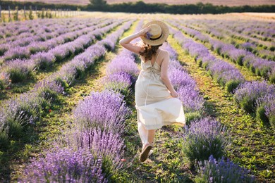 Photo of Woman with straw hat and beautiful flowers running through lavender field