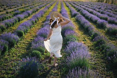 Photo of Woman with straw hat running through lavender field, back view