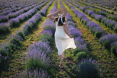 Photo of Woman with straw hat running through lavender field, back view