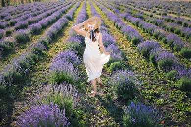 Photo of Woman in straw hat running through lavender field, back view