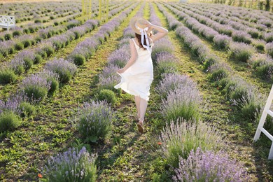 Photo of Woman in straw hat running through lavender field, back view