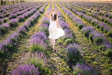 Photo of Woman in straw hat running through lavender field, back view