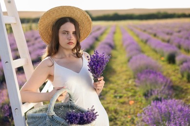 Photo of Beautiful young woman with lavender flowers and wicker basket in field