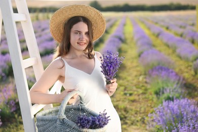 Photo of Beautiful young woman with lavender flowers and wicker basket in field