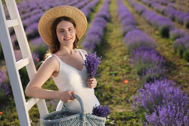 Photo of Beautiful young woman with lavender flowers and wicker basket in field
