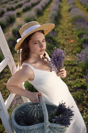 Photo of Beautiful young woman with lavender flowers and wicker basket in field