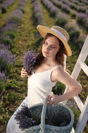Photo of Beautiful young woman with lavender flowers and wicker basket in field