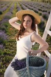 Photo of Beautiful young woman with lavender flowers and wicker basket in field