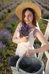 Photo of Beautiful young woman with lavender flowers and wicker basket in field
