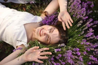 Photo of Beautiful young woman lying among lavender flowers outdoors, top view