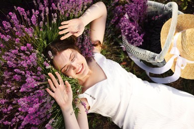 Photo of Beautiful young woman lying among lavender flowers outdoors, top view