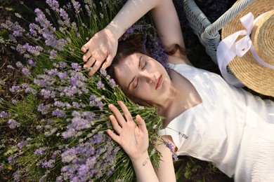 Photo of Beautiful young woman lying among lavender flowers outdoors, top view