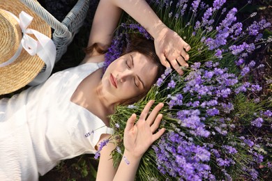Photo of Beautiful young woman lying among lavender flowers outdoors, top view