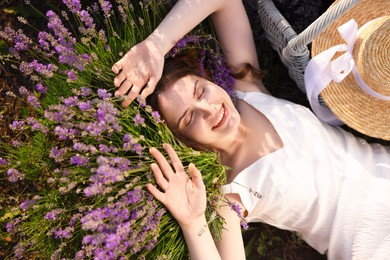 Photo of Beautiful young woman lying among lavender flowers outdoors, top view