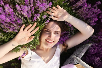 Photo of Beautiful young woman lying among lavender flowers outdoors, top view