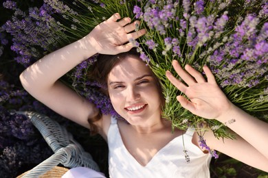 Photo of Beautiful young woman lying among lavender flowers outdoors, top view