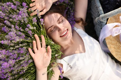 Photo of Beautiful young woman lying among lavender flowers outdoors, closeup