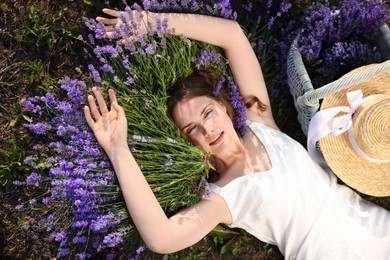 Photo of Beautiful young woman lying among lavender flowers outdoors, top view