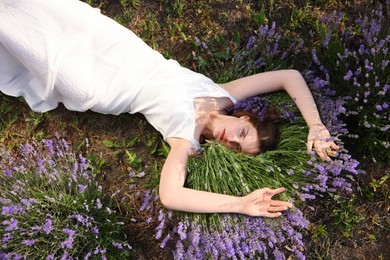 Photo of Beautiful young woman lying among lavender flowers outdoors, top view
