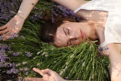 Photo of Beautiful young woman lying among lavender flowers outdoors, closeup