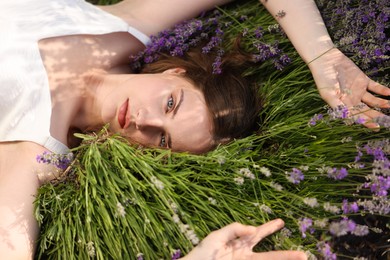 Photo of Beautiful young woman lying among lavender flowers outdoors, closeup