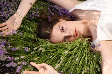 Photo of Beautiful young woman lying among lavender flowers outdoors, closeup