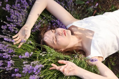 Photo of Beautiful young woman lying among lavender flowers outdoors, above view