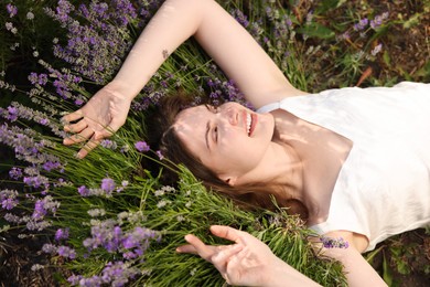 Photo of Beautiful young woman lying among lavender flowers outdoors, above view