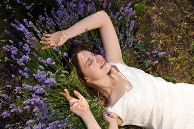 Photo of Beautiful young woman lying among lavender flowers outdoors, above view