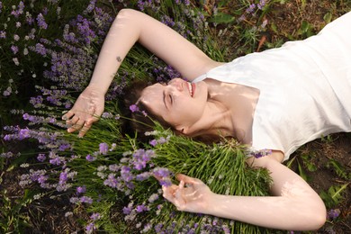 Photo of Beautiful young woman lying among lavender flowers outdoors, above view