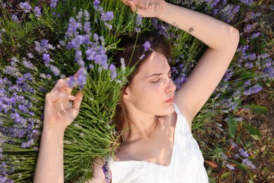 Photo of Beautiful young woman lying among lavender flowers outdoors, top view