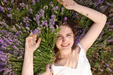 Photo of Beautiful young woman lying among lavender flowers outdoors, top view