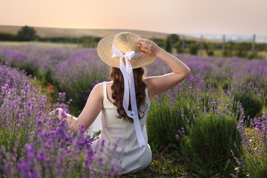 Photo of Woman with wicker hat sitting in beautiful lavender field, back view