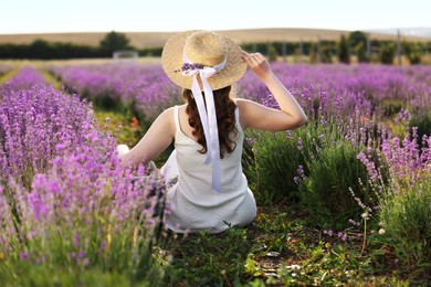 Photo of Woman with wicker hat sitting in beautiful lavender field, back view