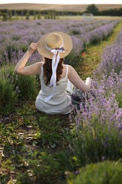 Photo of Woman with wicker hat sitting in beautiful lavender field, back view