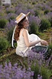 Photo of Beautiful young woman with wicker basket of lavender flowers sitting in field