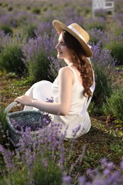 Photo of Beautiful young woman with wicker basket of lavender flowers sitting in field