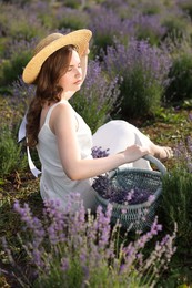 Photo of Beautiful young woman with wicker basket of lavender flowers sitting in field