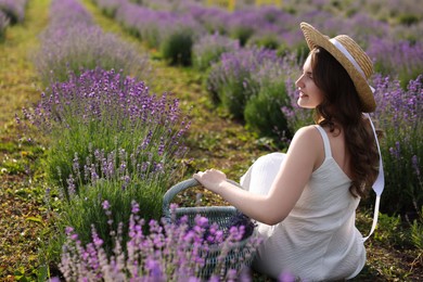 Photo of Beautiful young woman with wicker basket of lavender flowers sitting in field