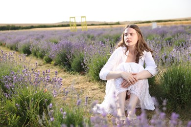 Photo of Beautiful young woman sitting among lavender flowers outdoors