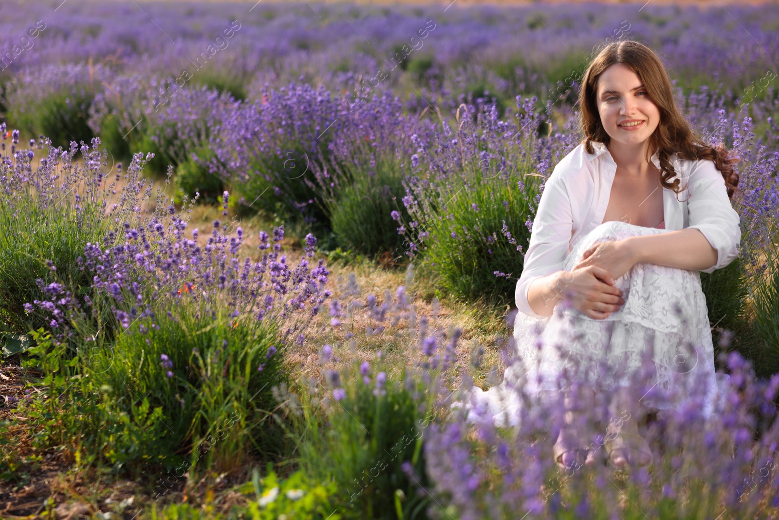 Photo of Beautiful young woman sitting among lavender flowers outdoors