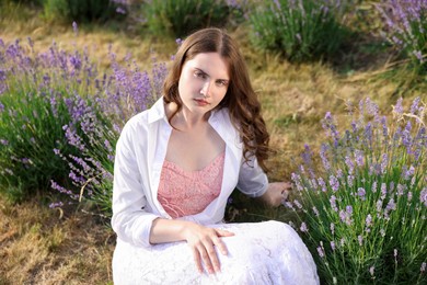 Photo of Beautiful young woman sitting among lavender flowers outdoors
