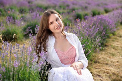 Photo of Beautiful young woman sitting among lavender flowers outdoors